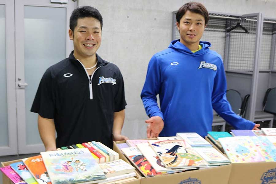 札幌ドームで来場者から回収した書籍と近藤選手、中島選手【画像提供：北海道日本ハムファイターズ】