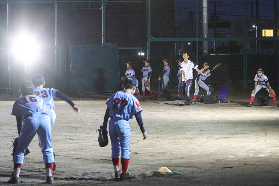 夜間照明の中でノックを打つ東16丁目フリッパーズ・笹谷武志監督【写真:石川加奈子】