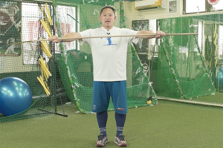 棒を使ったストレッチを実演する長坂秀樹氏【写真:編集部】